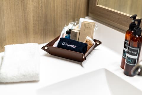 A bathroom countertop with a brown tray filled with cosmetics, a folded white towel, and bottles of lotion and soap.