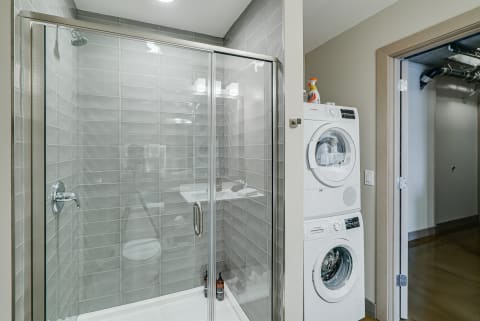 Compact bathroom showcasing a glass shower and a stacked washer and dryer.