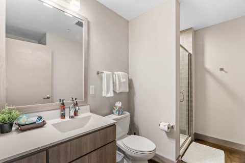 A contemporary bathroom featuring a white countertop, amber bottles, towels, and a glass shower.