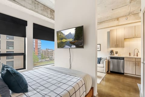 A stylish studio apartment with a bed, kitchen area, and large window.