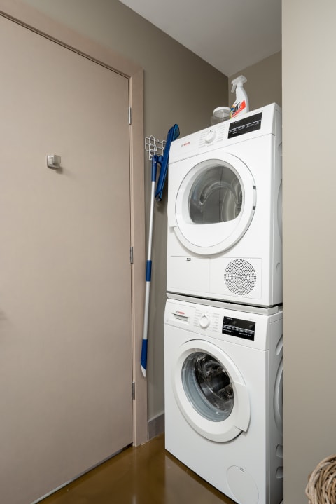 Compact laundry corner with a stacked washer and dryer, cleaning supplies, and a door.