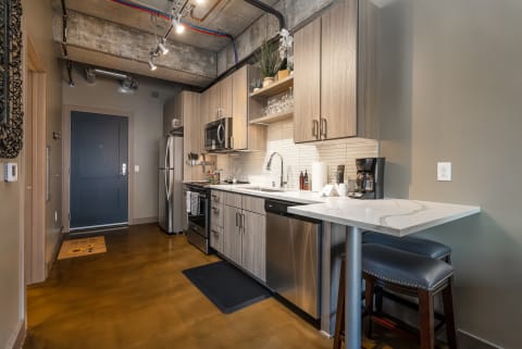 A contemporary kitchen featuring light cabinetry, stainless steel appliances, and a small breakfast bar with leather stools.