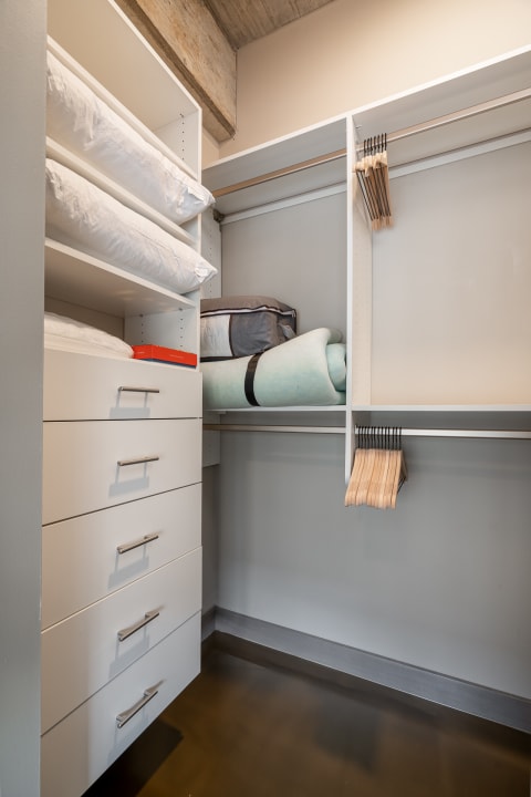 An organized closet with white shelves, pillows, and clothing hangers.