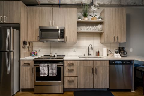 A contemporary kitchen featuring light wooden cabinetry, stainless steel appliances, and a clean white backsplash with small decor elements.