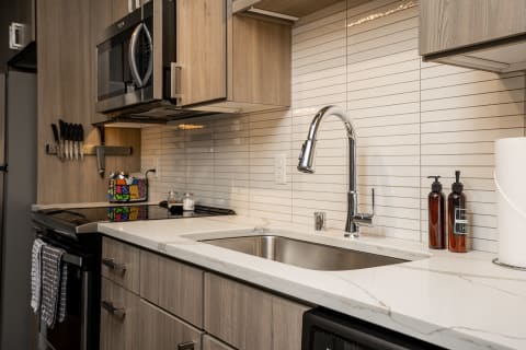 Modern kitchen with stainless steel sink, cabinets, and stove featuring a colorful kettle and neatly arranged utensils.