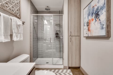 Modern bathroom with a glass shower, abstract art, and white towels.