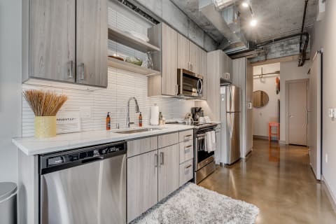 A contemporary kitchen with light wood cabinets, a marble countertop, and stainless steel appliances.