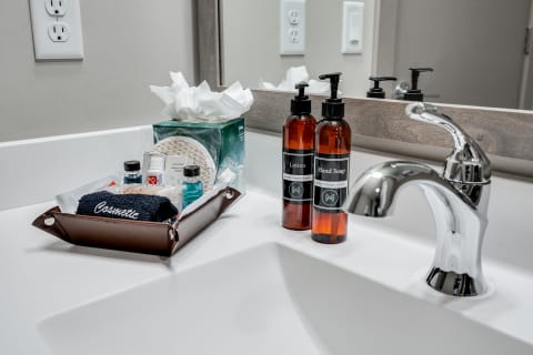 A bathroom vanity with a sink, hand soap and lotion bottles, tissues, and personal care items.