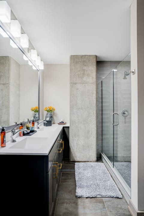 Modern bathroom with a black vanity, white countertop, glass shower, and decorative flowers.