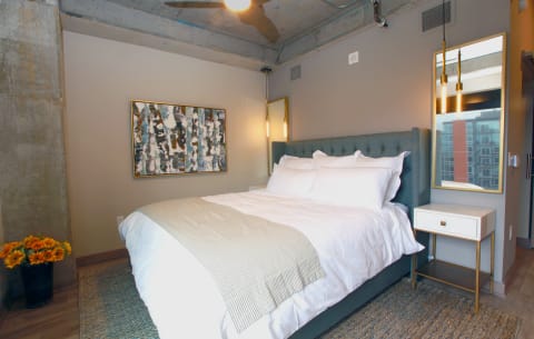 Modern bedroom with a tufted bed, abstract art, and sunflowers.