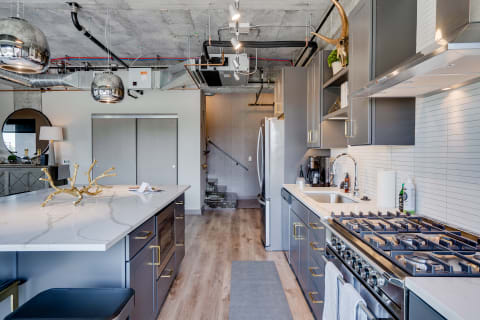 Contemporary kitchen with marble island, gray cabinets, and industrial ceiling lights.
