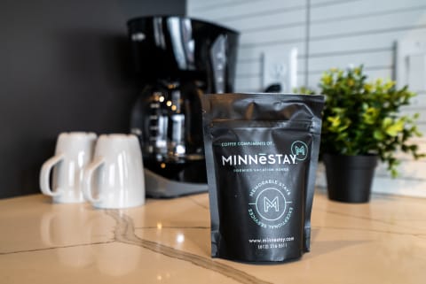 A bag of MINNESTAY coffee on a marble countertop with coffee mugs and a coffee maker in the background.