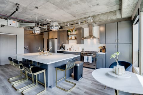 A modern kitchen with grey cabinets, marble island, and stainless steel appliances.