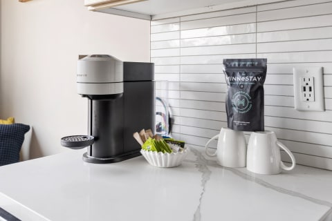 A coffee station with an espresso machine, white mugs, and condiments on a marble countertop.