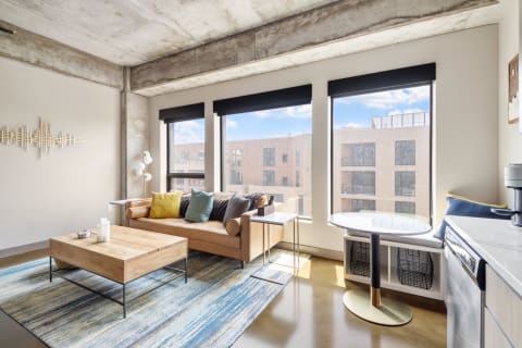 Modern living room with leather sofa, colorful cushions, and large windows.
