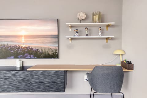 A clean and modern workspace featuring a desk, sunset photograph, and decorative items.