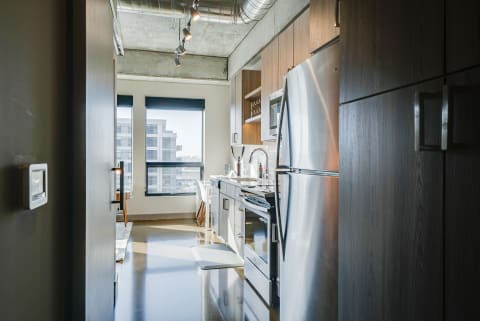 Modern kitchen with stainless steel appliances and a dining area, featuring a concrete ceiling and urban view.