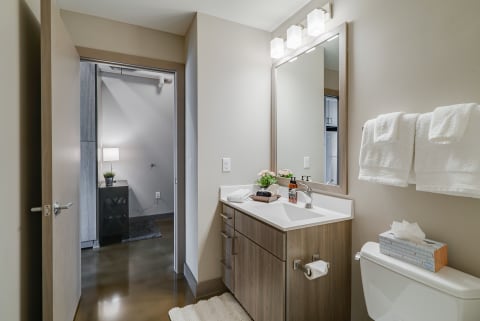 A contemporary bathroom featuring a wood vanity, white sink, and decorative items.