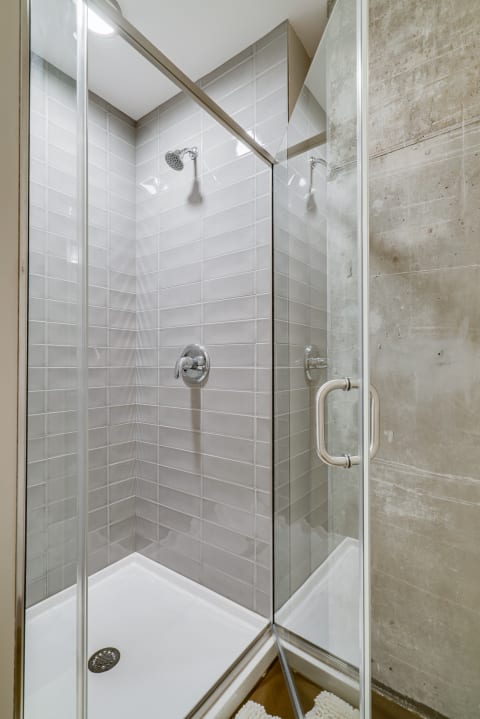 A spacious walk-in shower with glass doors and light gray tiled walls.