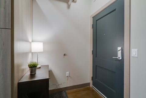 A contemporary entryway featuring a dark door, wooden console table, lamp, and potted plant.