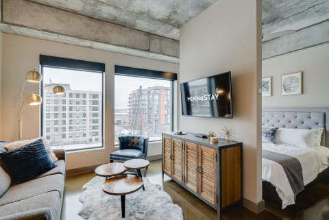 Modern studio apartment featuring a gray sofa, television, and a cozy bed.