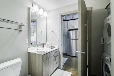 Interior view of a modern bathroom featuring a wooden vanity, mirror, and laundry area.