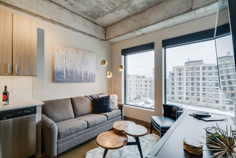Modern living room with a gray sofa, abstract artwork, and large windows overlooking a snowy cityscape.