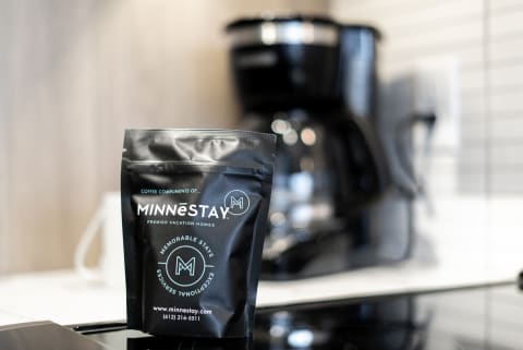 A black coffee bag labeled Minnēstay in a contemporary kitchen with a coffee maker in the background.