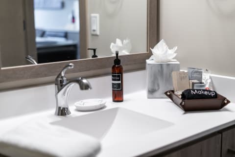 Modern bathroom sink with hand soap, tissues, and makeup products.