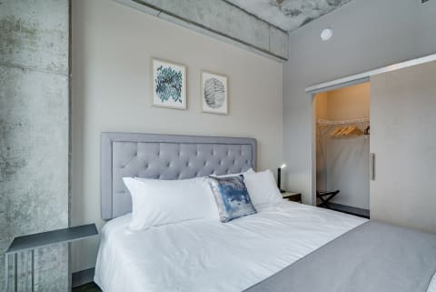 A modern bedroom featuring a grey tufted headboard, white linens, and industrial touches.