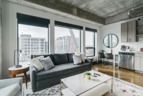 A stylish living space featuring a gray sofa, large windows, and a sleek kitchen.