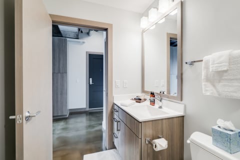 Interior view of a contemporary bathroom featuring a light wood vanity, large mirror, and polished concrete floors.