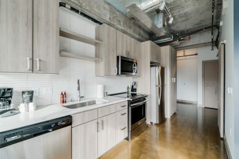 Contemporary kitchen featuring stainless steel appliances, light wood cabinets, and polished concrete flooring.