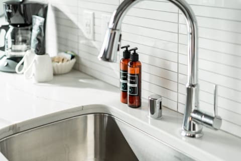 A contemporary kitchen sink with soap bottles and a coffee maker in the background.