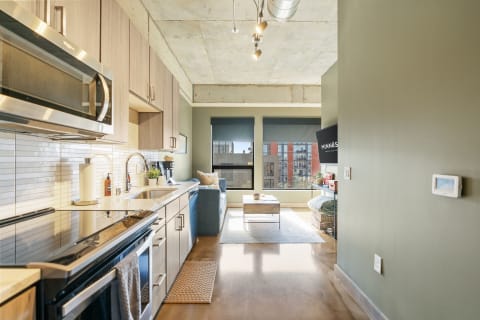 Modern studio apartment kitchen and living area with blue sofa and natural light.
