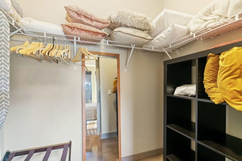 An organized closet with cushions on a shelf, hangers on display, and a mirror.