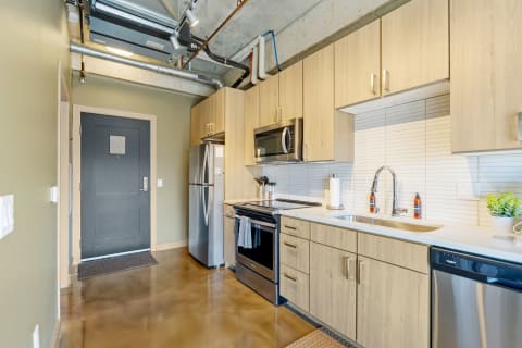 Contemporary kitchen featuring wooden cabinets, stainless steel appliances, and a dark blue door.