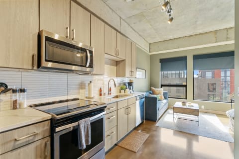 Compact modern apartment kitchen and living area with stainless steel appliances and natural light.