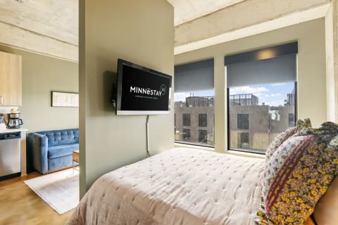 Modern bedroom interior with bed, blue sofa, and flat-screen TV.