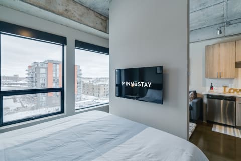 Modern bedroom with a bed, TV displaying MINNESTAY, and a snowy view outside.