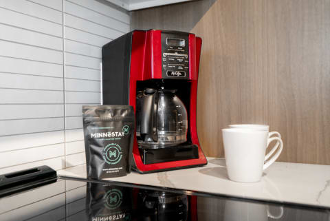 A red coffee maker, a bag of coffee, and two white mugs on a kitchen countertop.