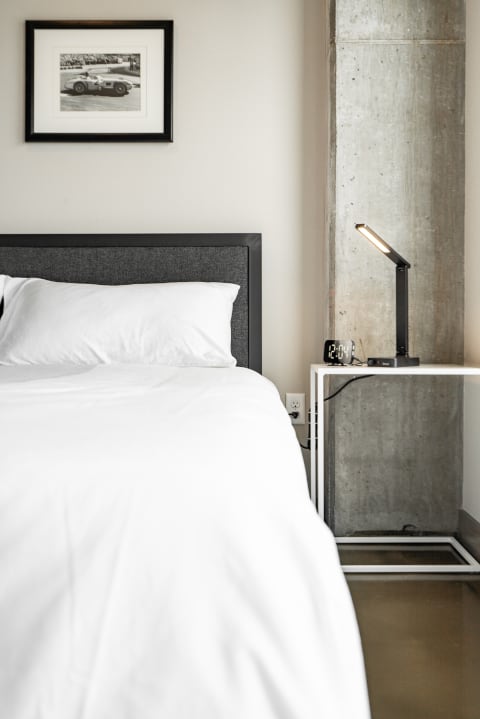 Minimalistic bedroom with white bed linens, gray headboard, and a framed photograph.