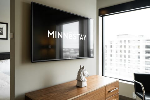 Contemporary hotel room with MINNēSTAY logo on TV, wooden dresser, and horse sculpture.