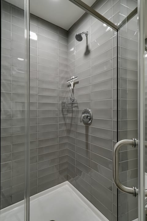 Modern shower space with gray tiles and a whimsical squeegee figure.