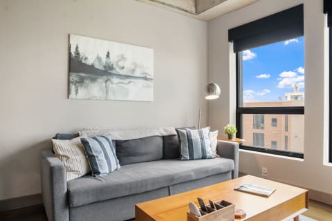 Modern living room with a gray sofa, abstract painting, and large windows.