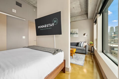 Contemporary studio apartment featuring a bed, TV, and seating area with city views.