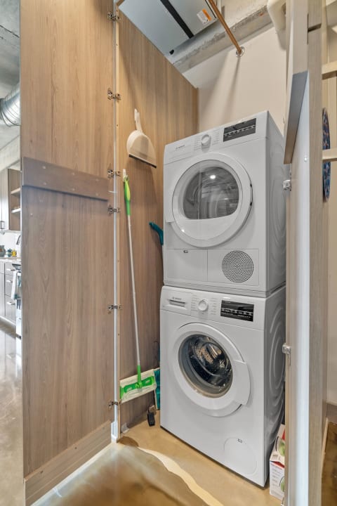 A compact laundry corner featuring a stacked washing machine and dryer with wooden panels in the background.