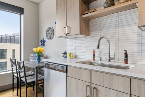 A contemporary kitchen featuring a dining area with yellow tulips, gray cabinets, and a large window.