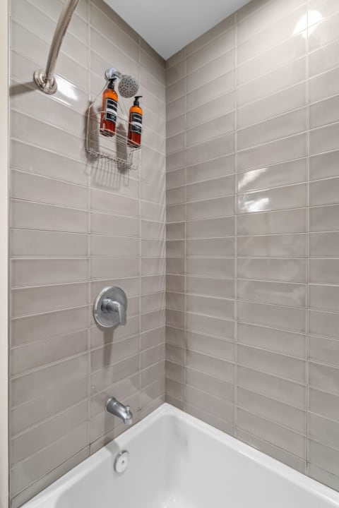 Shower area featuring beige tiles, a curved showerhead, and bottles of body wash.
