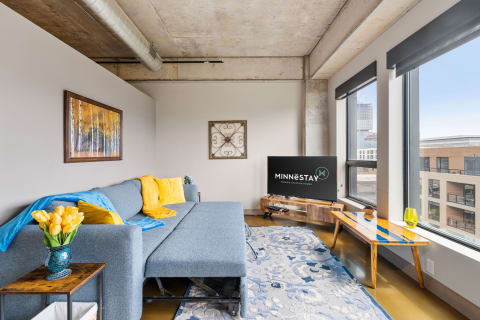 Modern living room with a gray sofa, colorful pillows, wooden furniture, and a view of the outdoors.